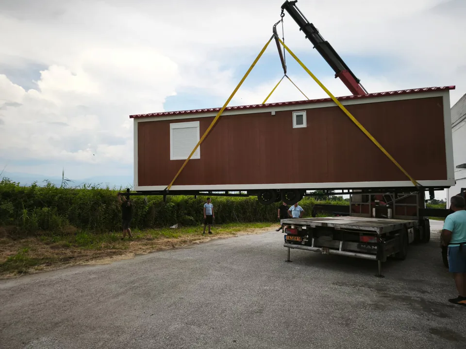 Crane lifting a wood-look mobile home to load it onto a truck
