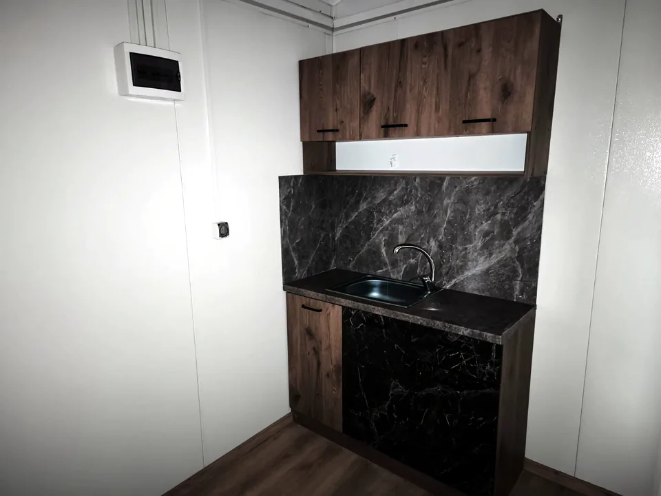Mobile home kitchen with timber cabinets, a black marble-look splashback and a steel sink