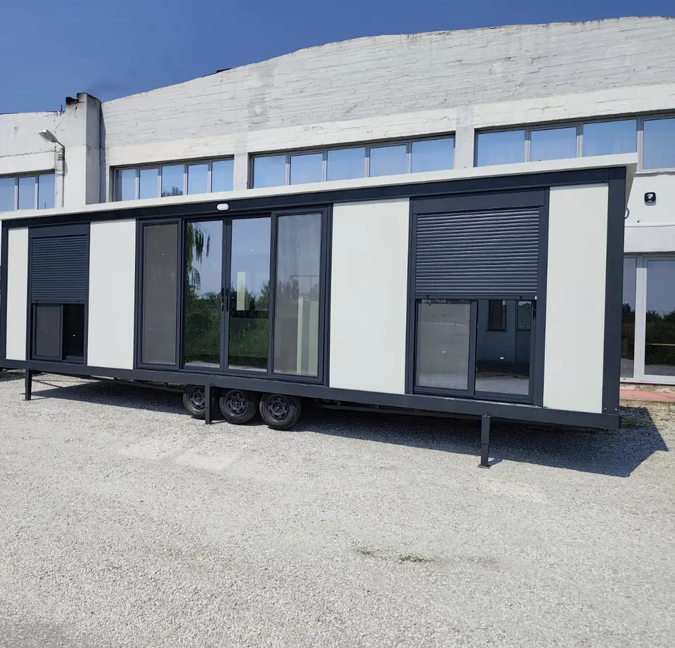 Triple-axle Modern Line mobile home with a sliding glass door and roller shutters, in the factory yard