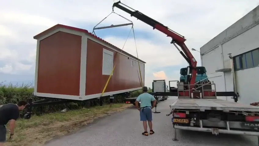 Crane lifting a wood-look mobile home onto a truck platform