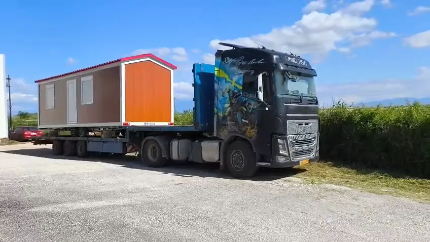 Truck with a mobile home on its trailer pulling up on a road beside fields